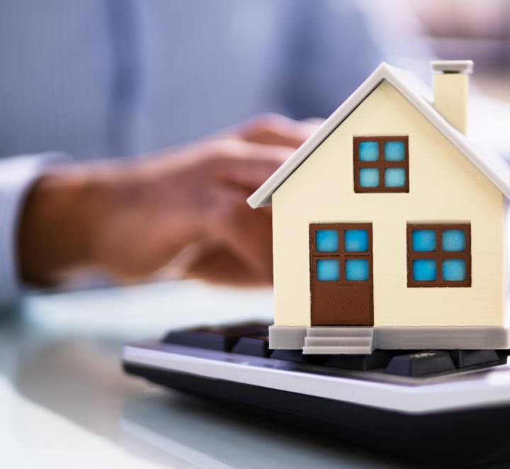 Man working at desk with small model of house on calculator