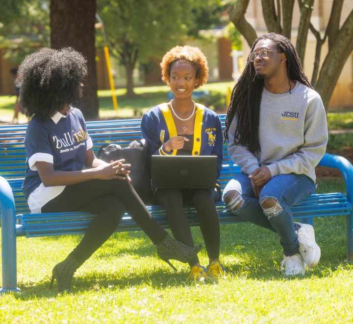 Three students on a bench with a laptop