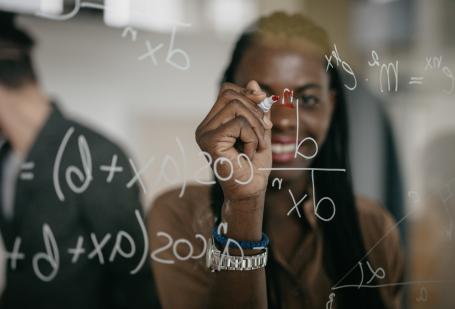 Woman solving equations on glass wall in front of camera