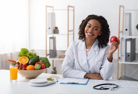 Woman in lab coat holding an apple.