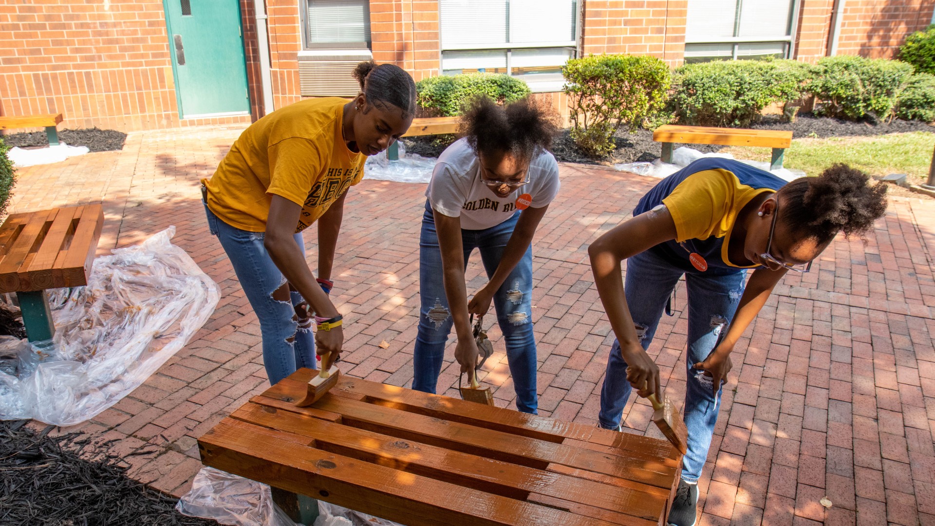 Three student volunteers painting a bench